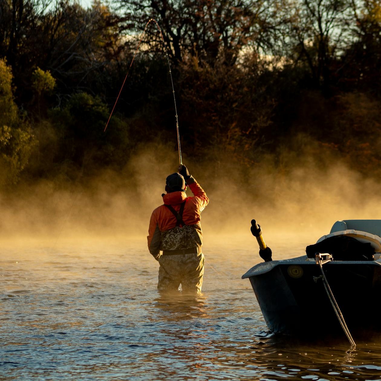 Fisherman casting in misty dawn light on river