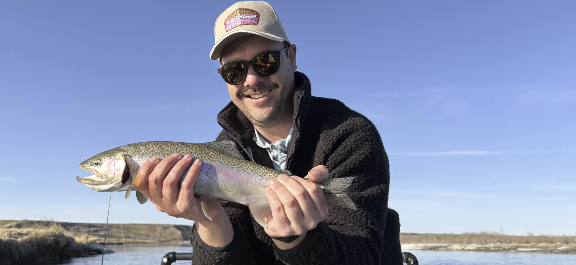 Smiling guest holding a Bow River rainbow trout under a bluebird sky on a guided fly fishing trip with King Trout Outfitters near Calgary